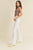 Woman wearing a brown crop top and white flared pants on a beige background