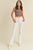 Woman wearing a brown sleeveless top and white flared jeans on a beige background