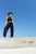 Person wearing a black outfit standing on a concrete ledge with a clear blue sky in the background
